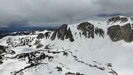 Below left is Mirror Lake, Lake Marie is further behind - and below the cliff right is a snowed-over Lookout Lake. A storm is visible on the horizon.